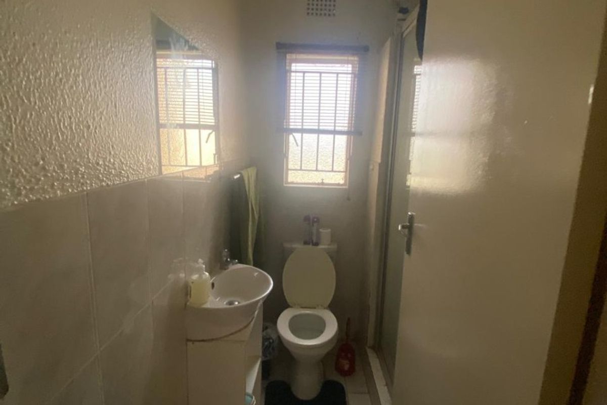 A compact bathroom featuring a pedestal basin, toilet, and shower enclosure with tiled flooring and wall finishes.