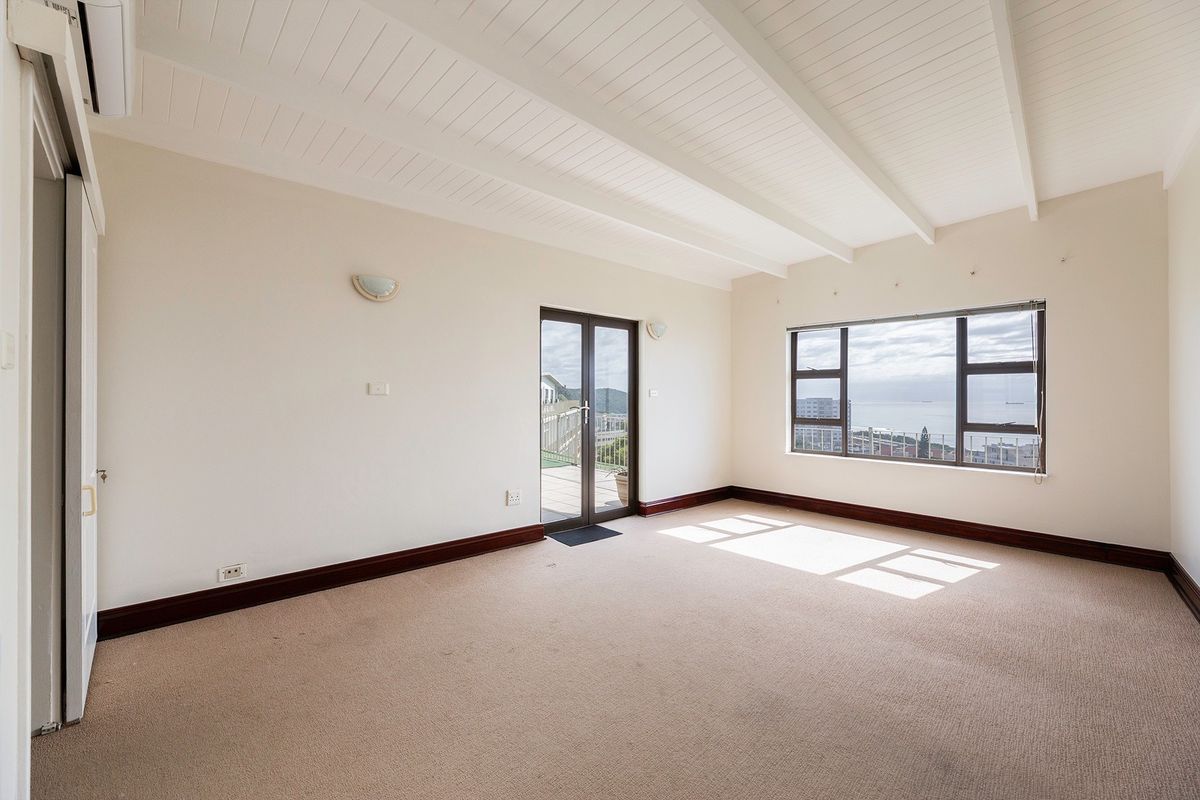 Spacious living area featuring exposed beam ceilings, neutral carpeting, and large windows offering natural light and scenic views, with direct access to a balcony.