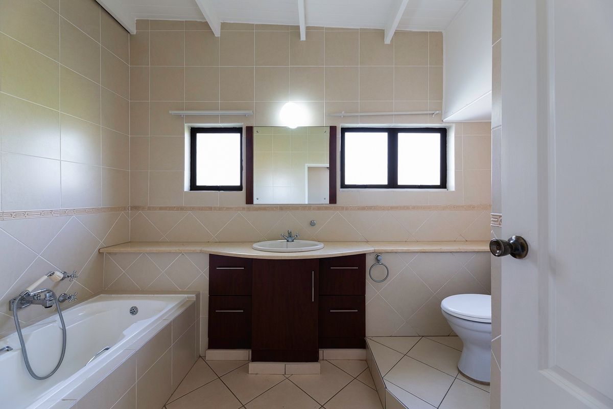 A functional bathroom featuring a built-in vanity with basin, a bathtub with shower mixer, and a toilet, finished with neutral wall and floor tiles.