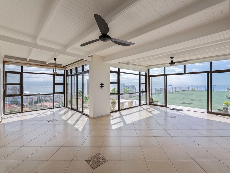 Spacious covered balcony featuring tiled flooring, exposed beam ceilings, ceiling fans, and expansive glass sliding doors offering panoramic coastal views.