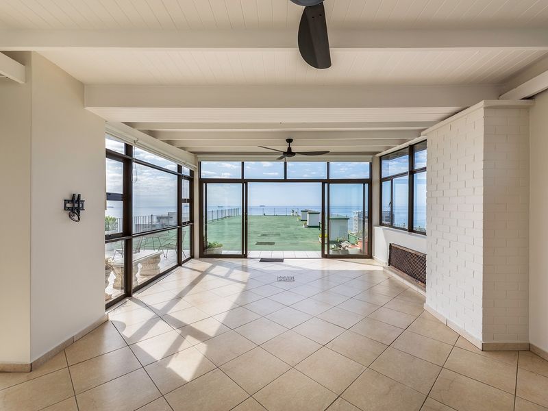 Spacious enclosed balcony featuring tiled floors, exposed beam ceilings, ceiling fans, and large sliding glass doors offering expansive ocean views.