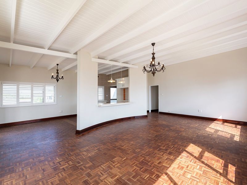 Spacious open-plan living area featuring classic parquet flooring, exposed beam ceilings, and a convenient pass-through window connecting to the kitchen.