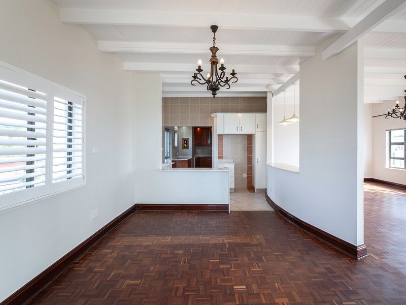 Spacious open-plan living and kitchen area featuring classic parquet flooring, exposed beam ceilings, and plantation shutters, offering a bright and versatile layout.