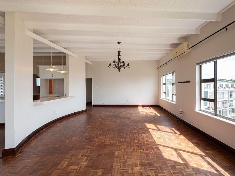 Spacious open-plan living area featuring beautiful parquet flooring, exposed beam ceilings, and a breakfast bar connecting to the kitchen, filled with natural light.