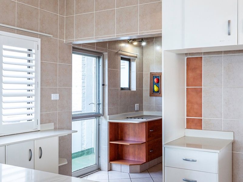 A clean, functional kitchen featuring tiled walls and flooring, ample built-in cabinetry, and a separate scullery area with a hob.