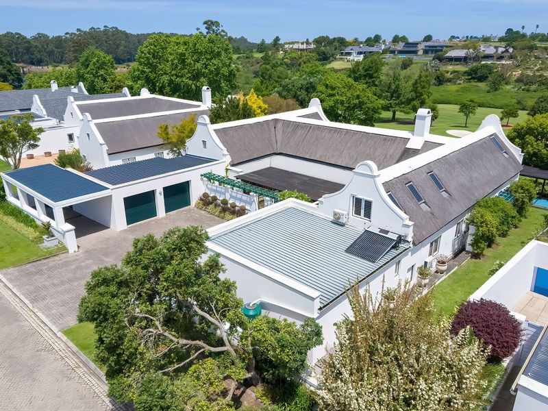 Aerial view of a well-maintained Cape Dutch style residence featuring a thatched roof, double garage, and landscaped grounds in a scenic estate setting.