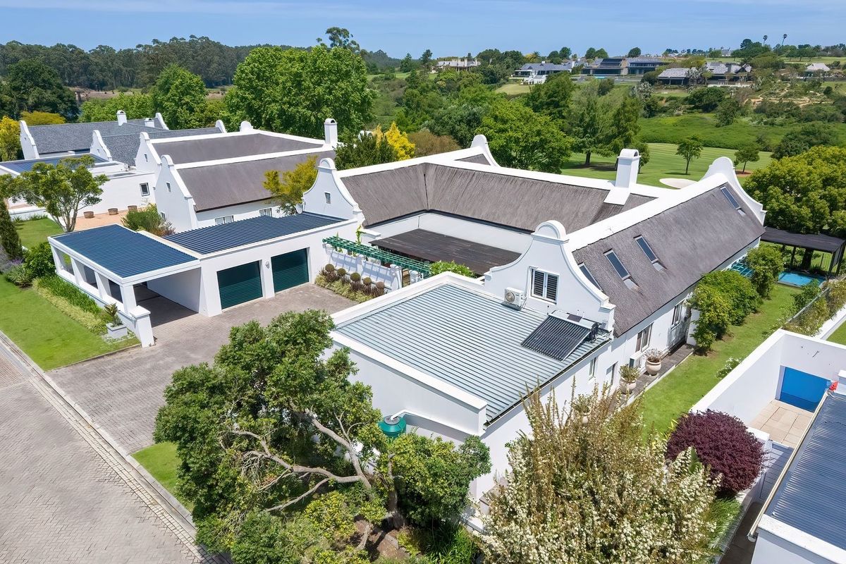 Aerial view of a well-maintained Cape Dutch style residence featuring a thatched roof, double garage, and landscaped grounds in a scenic estate setting.