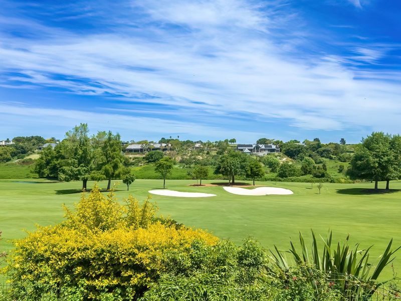 A scenic elevated view overlooking a well-maintained golf course with lush green fairways and sand bunkers under a clear blue sky.