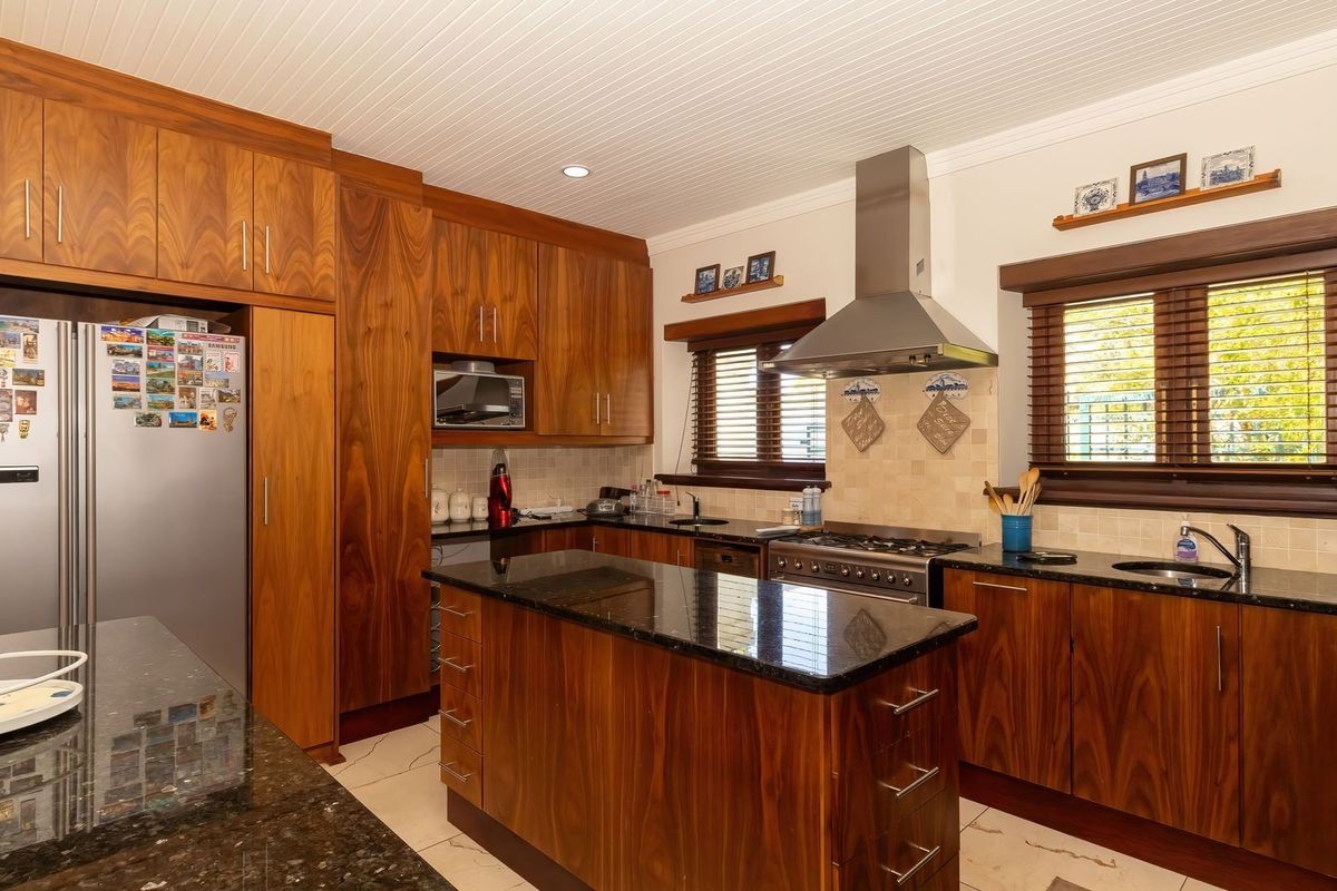 A well-appointed kitchen featuring rich wooden cabinetry, granite countertops, a stainless steel extractor fan, and a gas cooktop with a tiled backsplash.