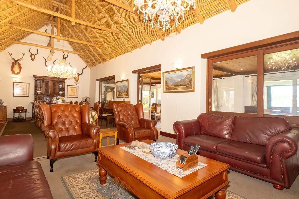 Spacious living room featuring a high exposed thatch ceiling with timber trusses, large sliding glass doors, and elegant chandelier lighting.