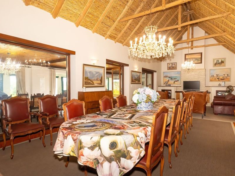 Spacious dining room featuring a high exposed thatch ceiling with timber trusses, a stone-clad fireplace, and a large feature mirror.