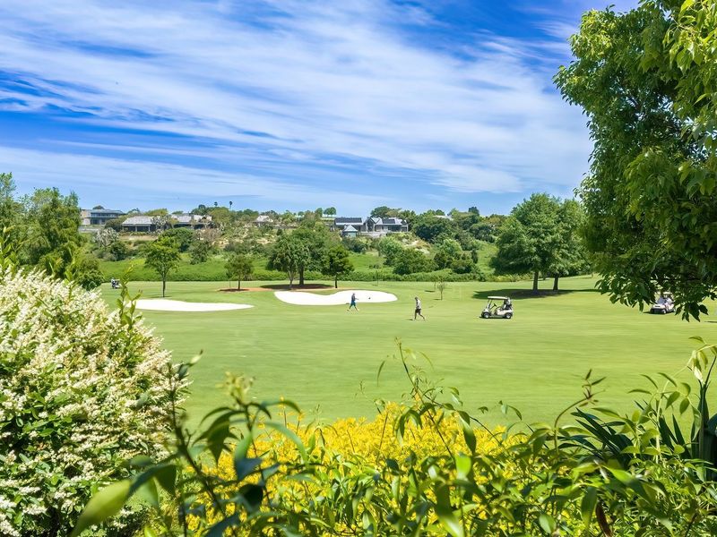 A scenic view overlooking a well-maintained golf course with lush green fairways and sand bunkers under a clear blue sky.