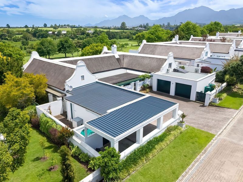 Aerial view of a well-maintained residential property featuring a thatched roof, double garage, private swimming pool, and landscaped garden in a scenic estate setting.