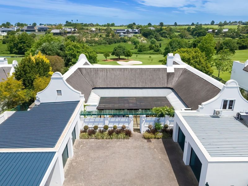 Aerial view of a well-maintained property featuring a traditional thatched roof, paved driveway, multiple garages, and a scenic outlook over a golf course.