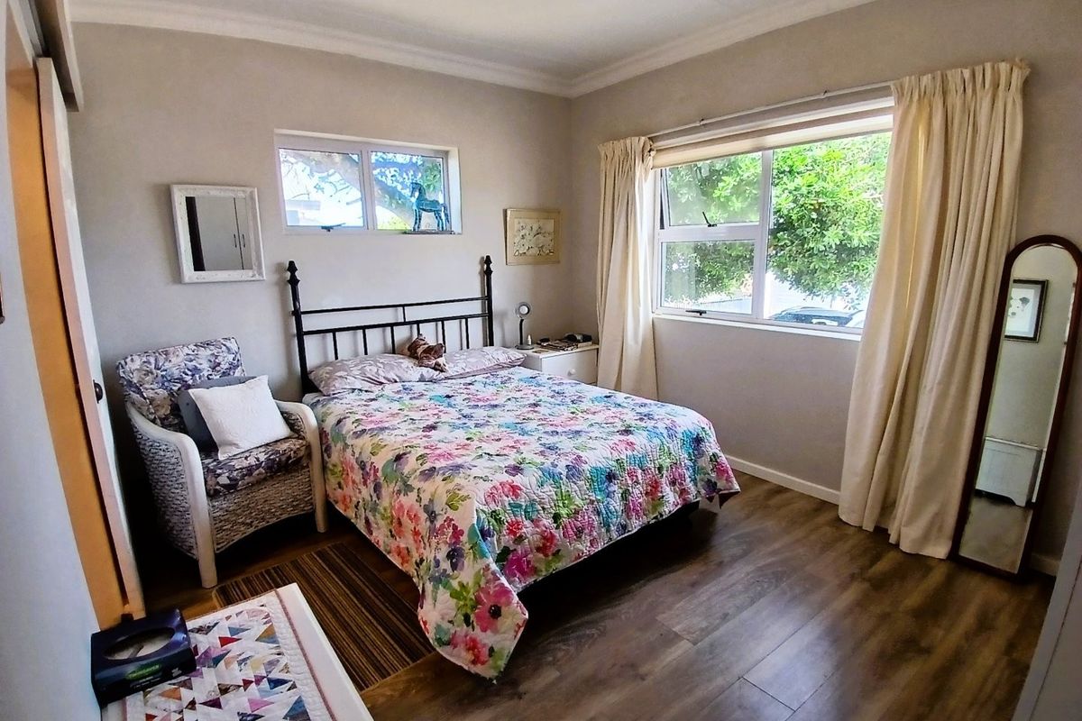 A well-lit bedroom featuring laminate flooring, neutral wall tones, and large windows that provide natural light and garden views.
