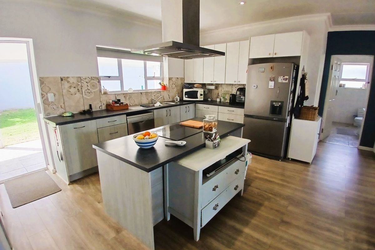 A functional kitchen featuring a central island, modern cabinetry, stainless steel extractor fan, and durable laminate flooring with direct access to the outdoor area.