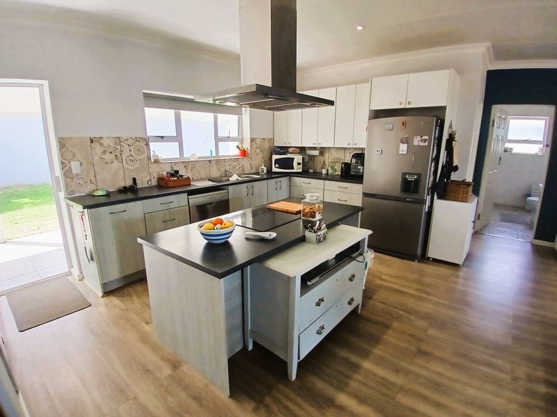 A functional kitchen featuring a central island, modern cabinetry, stainless steel extractor fan, and durable laminate flooring with direct access to the outdoor area.