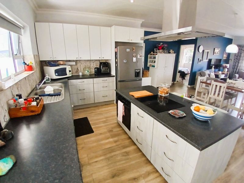 Open plan kitchen featuring a central island with integrated cooktop, modern cabinetry, and durable laminate flooring, seamlessly connecting to the adjacent living and dining areas.
