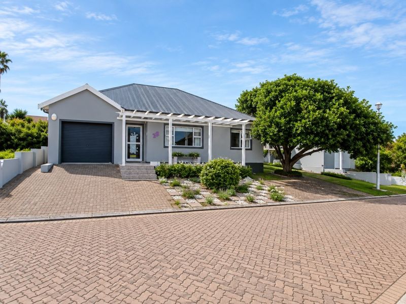 A well-maintained single-story house featuring a paved driveway, integrated garage, and a front pergola, set in a neat residential street.