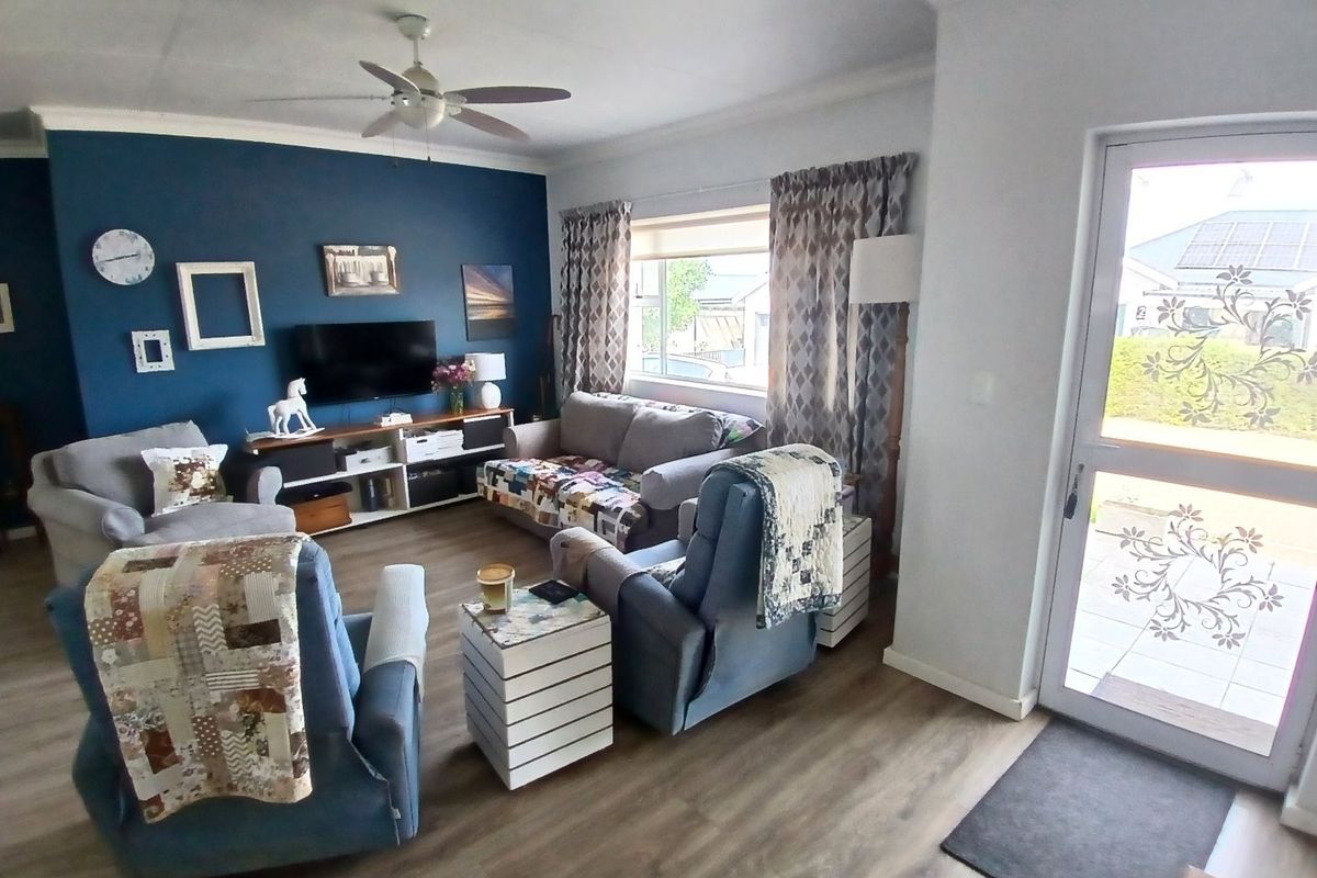 A comfortable living room featuring laminate flooring, a ceiling fan, and a glass-panelled entrance door, creating a bright and welcoming space.