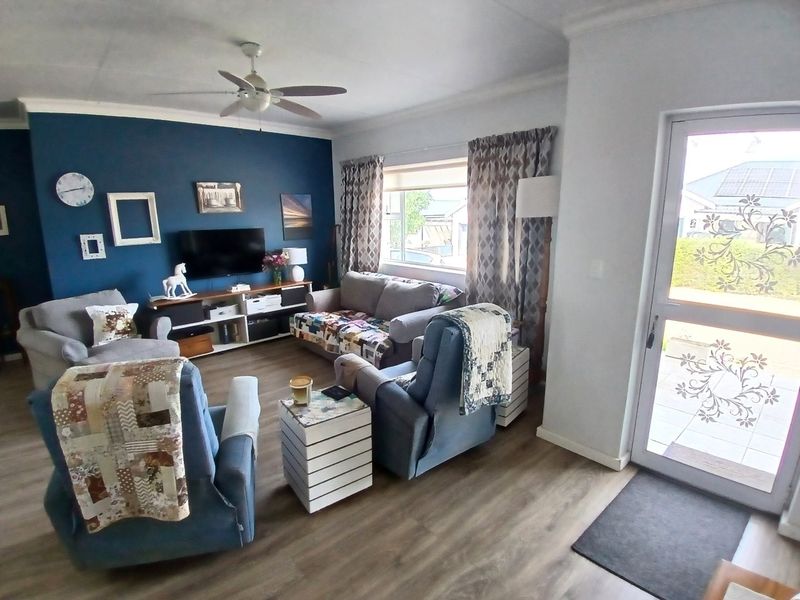 A comfortable living room featuring laminate flooring, a ceiling fan, and a glass-panelled entrance door, creating a bright and welcoming space.