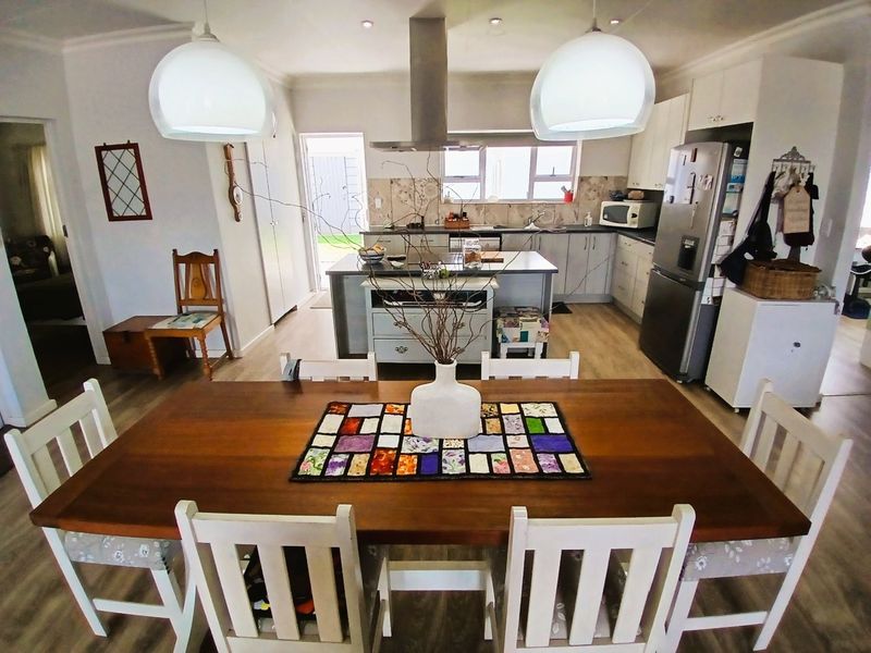 Open plan kitchen and dining area featuring a central island, modern cabinetry, tiled backsplash, and laminate flooring with integrated lighting.