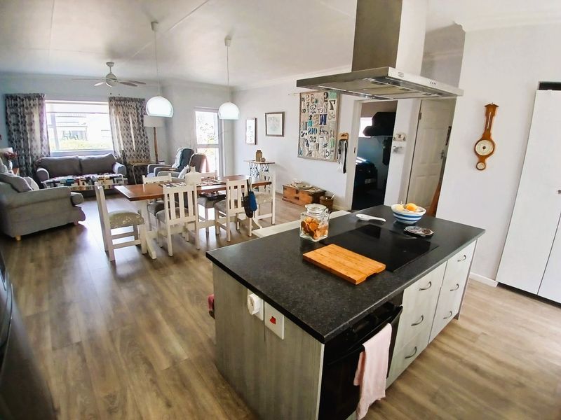 Spacious open-plan living and dining area featuring a central kitchen island with built-in hob and extractor fan, complemented by modern laminate flooring throughout.