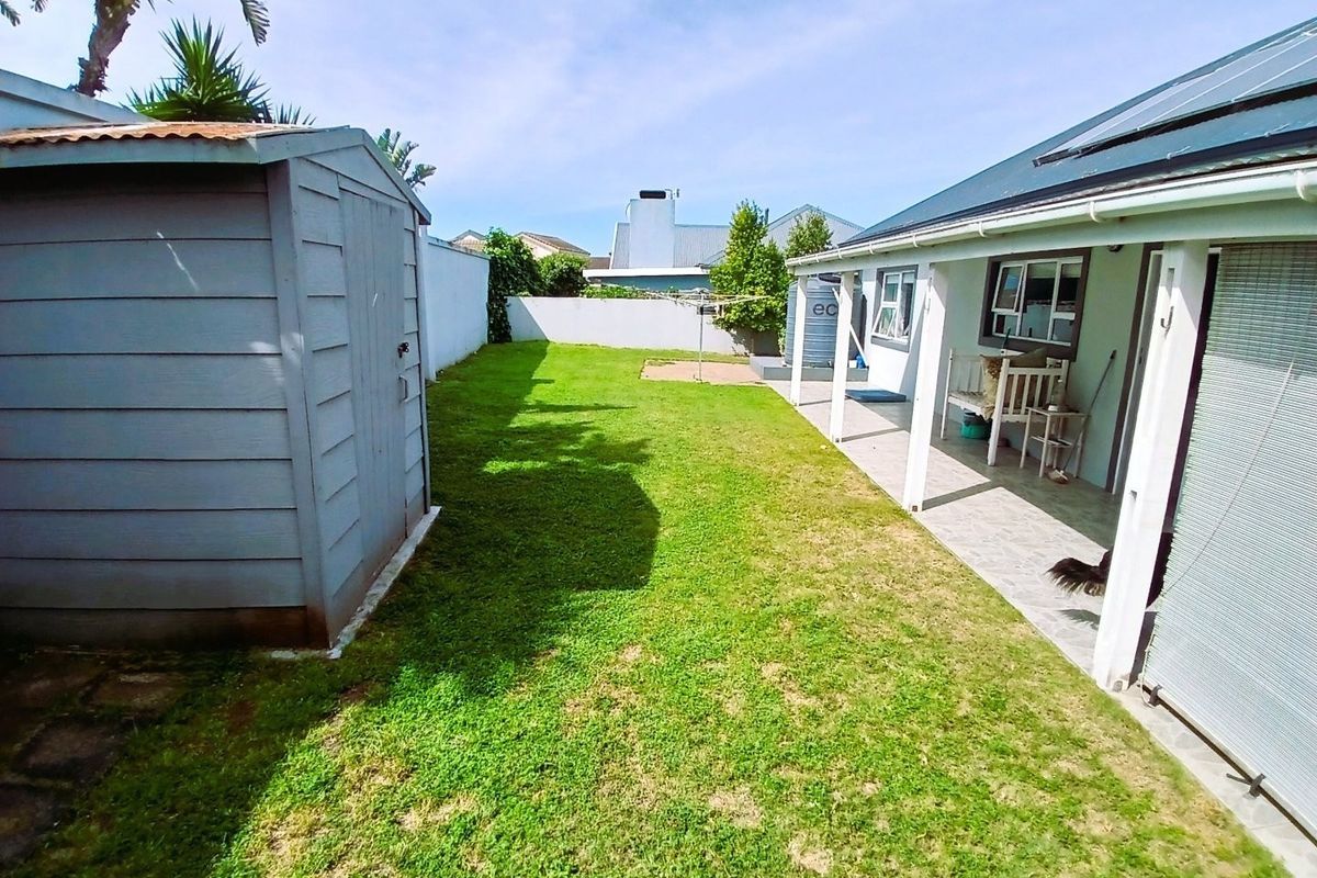 Rear garden featuring a lawn, covered patio area, garden shed, and boundary walling, providing a functional outdoor space.