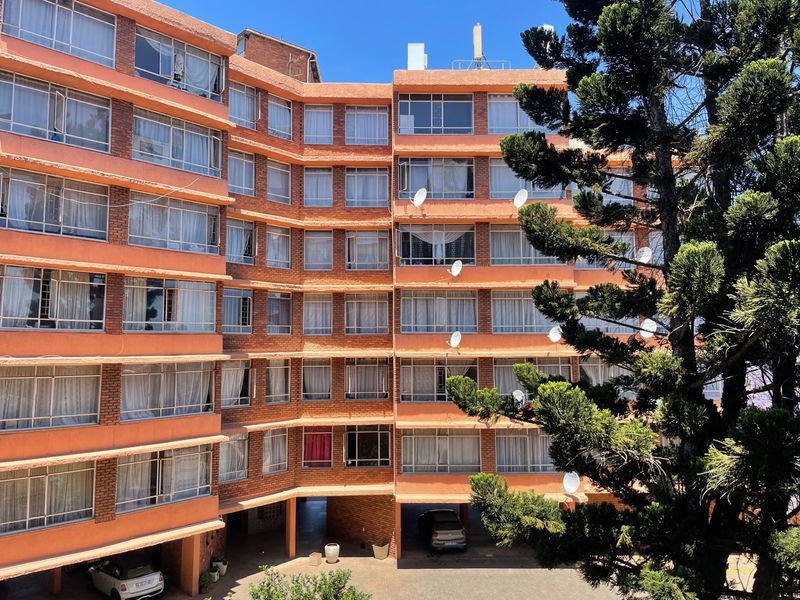 A multi-story apartment building featuring a brick facade, numerous windows, and a ground-level covered parking area.