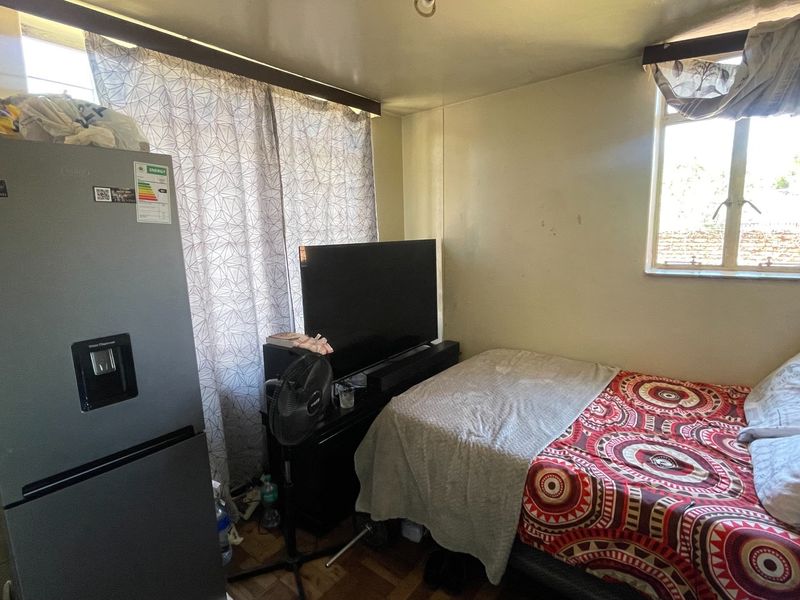 A compact bedroom featuring parquet flooring and a casement window, currently utilized as a multi-purpose living space.