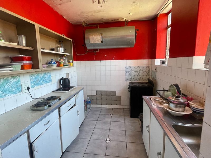 A dated kitchen featuring built-in cabinetry, a stainless steel sink, and tiled finishes, currently requiring significant maintenance and cosmetic updates.