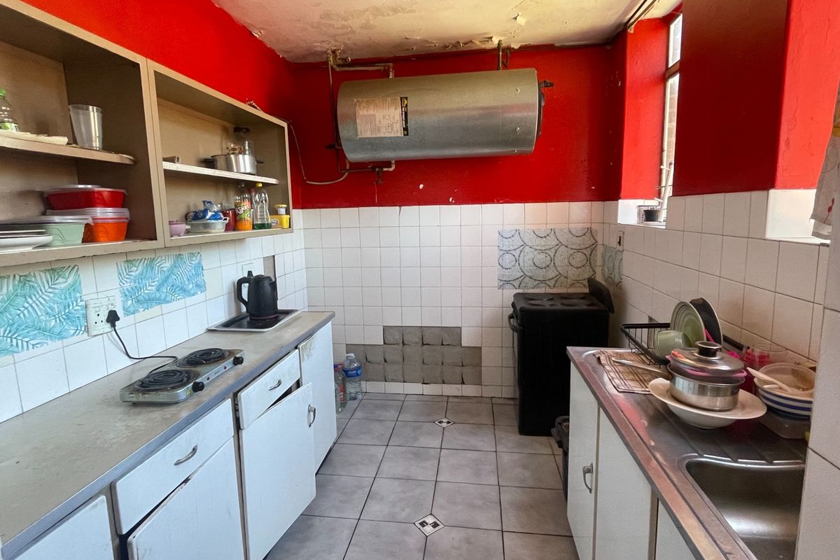 A dated kitchen featuring built-in cabinetry, a stainless steel sink, and tiled finishes, currently requiring significant maintenance and cosmetic updates.