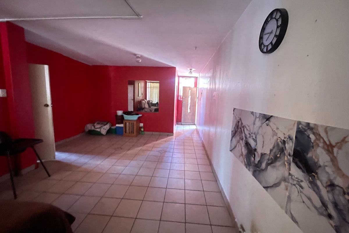A spacious living area featuring tiled flooring and a unique internal window, offering a blank canvas for potential interior design updates.
