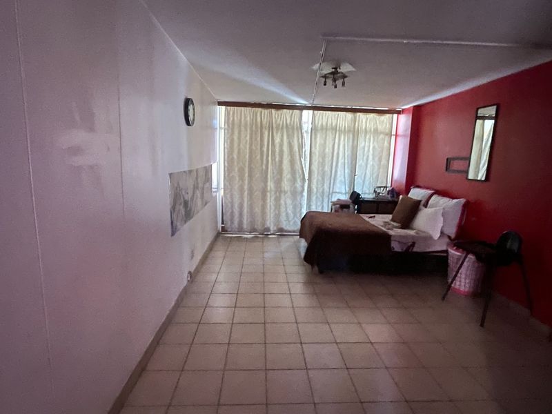 A spacious bedroom featuring tiled flooring and a large window with curtains, offering a blank canvas for potential interior updates and modernization.