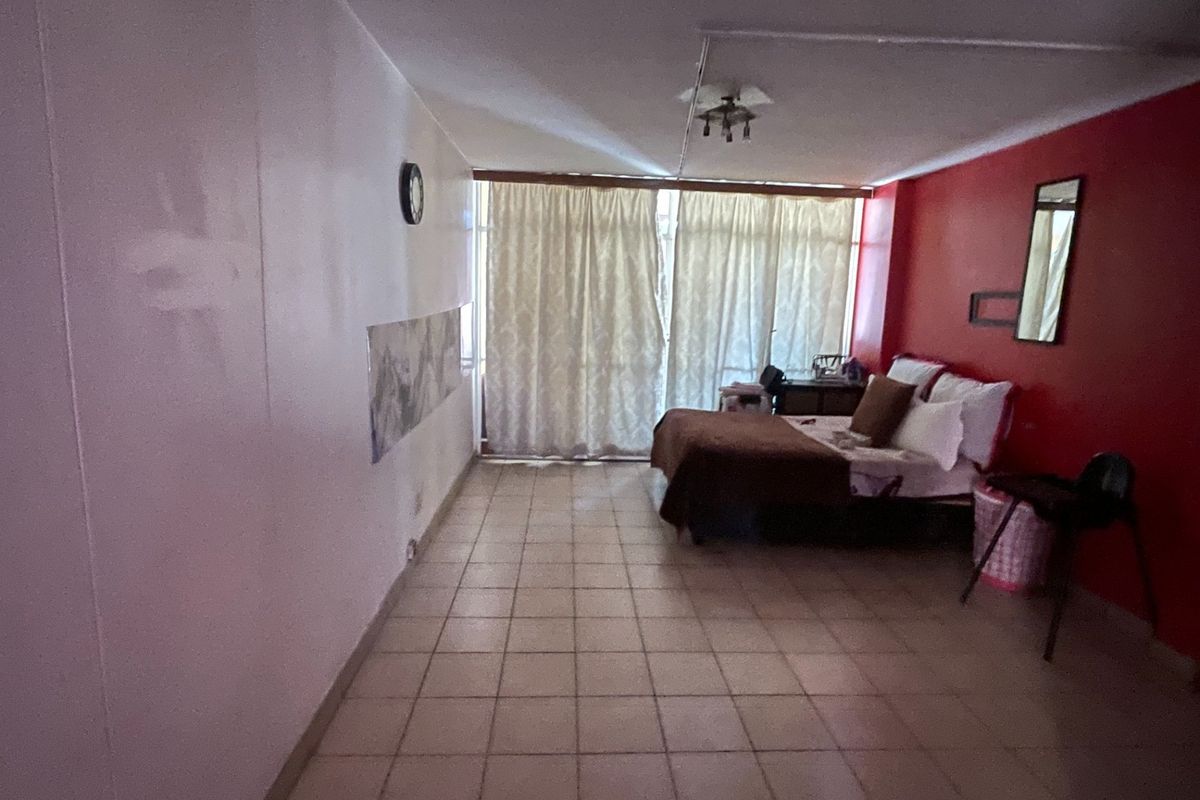 A spacious bedroom featuring tiled flooring and a large window with curtains, offering a blank canvas for potential interior updates and modernization.