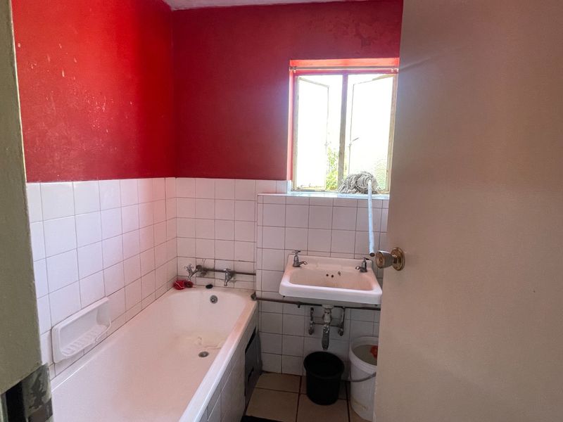 A dated bathroom featuring a bathtub, wall-mounted basin, and tiled finishes, requiring cosmetic updates to modernize the space.