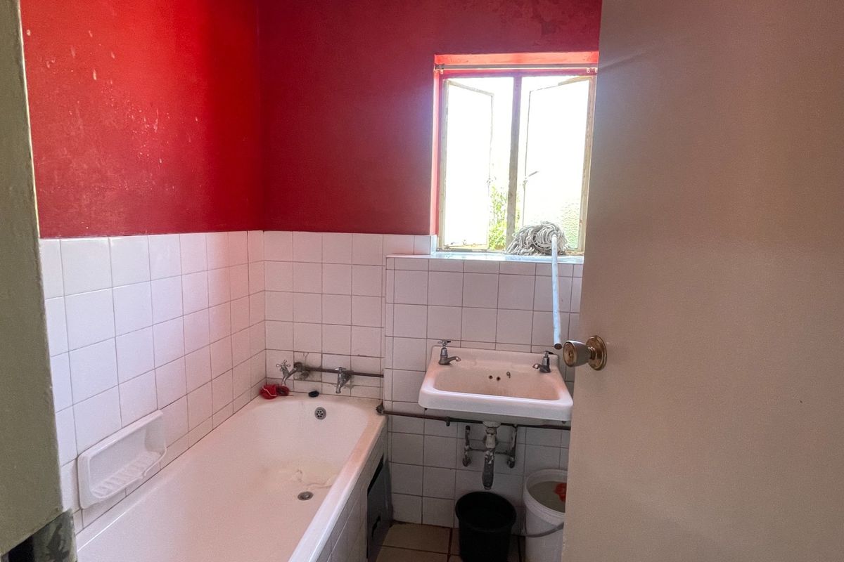 A dated bathroom featuring a bathtub, wall-mounted basin, and tiled finishes, requiring cosmetic updates to modernize the space.