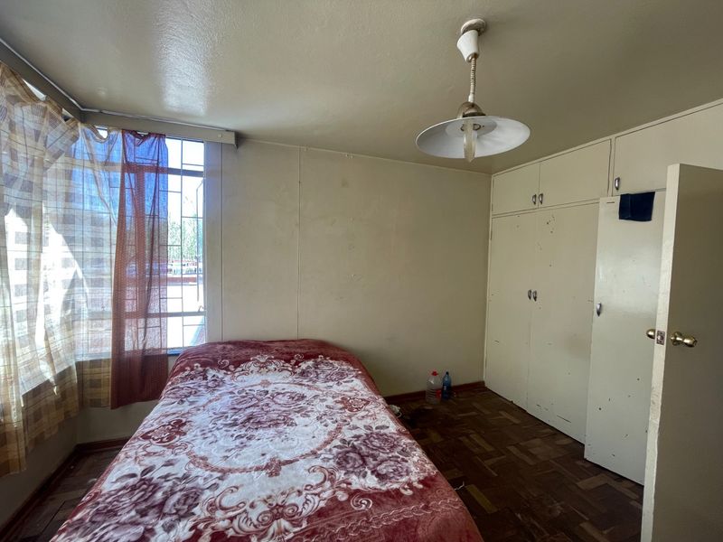 A bedroom featuring parquet flooring, built-in cupboards, and security bars on the window. The space requires cosmetic updates to improve its overall condition.
