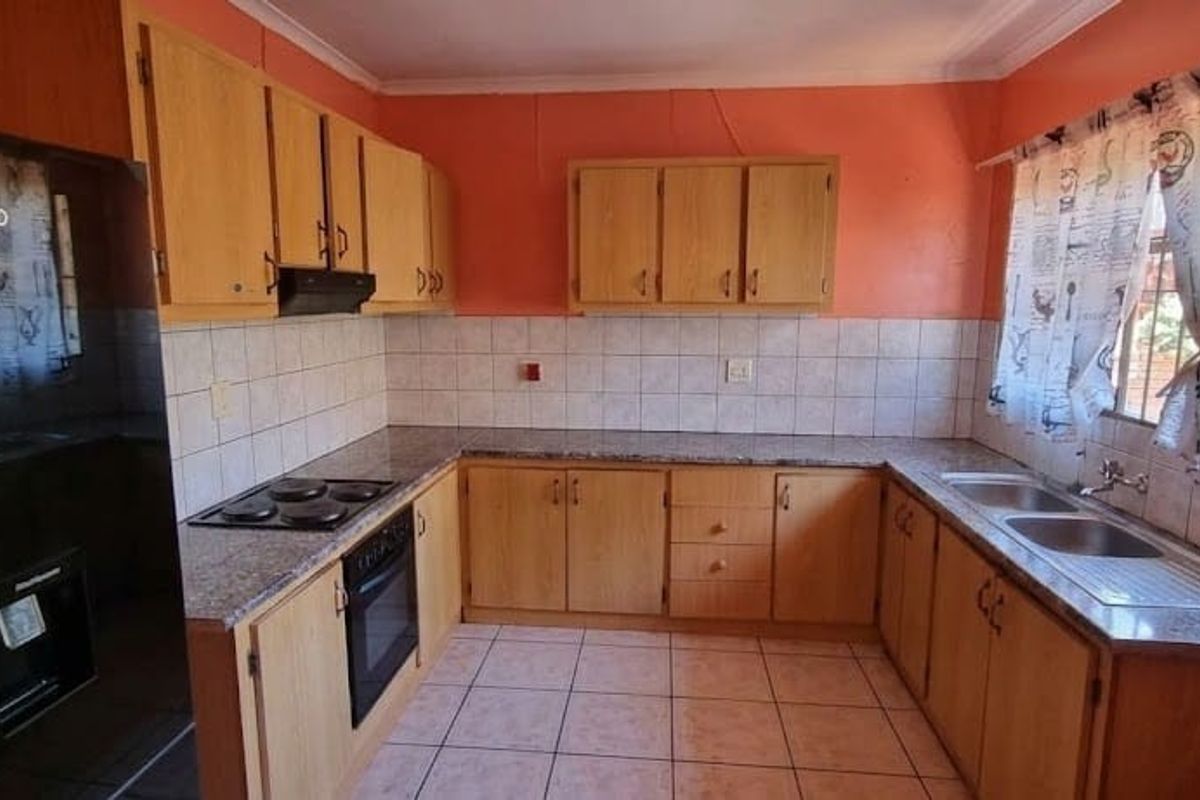 A dated kitchen featuring wooden cabinetry, laminate countertops, built-in oven and hob, and tiled splashbacks, offering potential for a modern renovation.