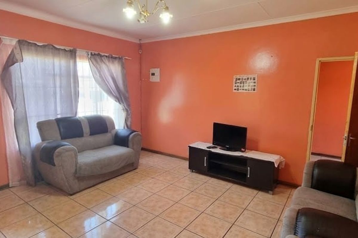A living room featuring tiled flooring and orange wall finishes, providing a functional space with direct access to adjacent areas.
