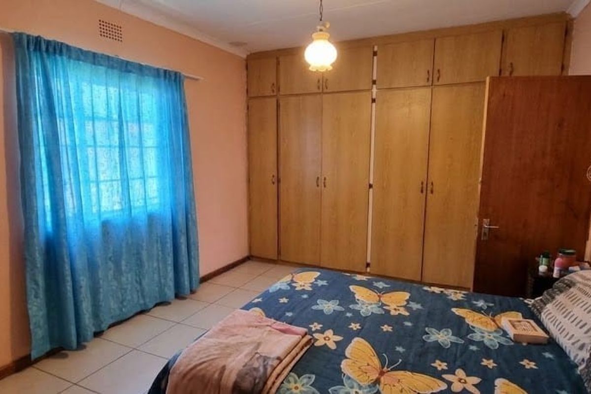 A bedroom featuring tiled flooring, a window with security bars, and extensive built-in wooden cupboards providing ample storage space.