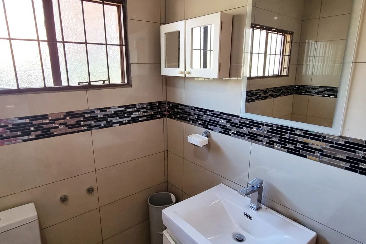 A functional bathroom featuring neutral wall tiles with a decorative mosaic border, a modern basin with chrome mixer, and a wall-mounted vanity cabinet.