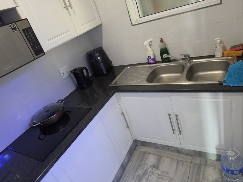 A functional kitchen featuring white cabinetry, dark granite countertops, a double stainless steel sink, and a built-in electric hob with microwave.