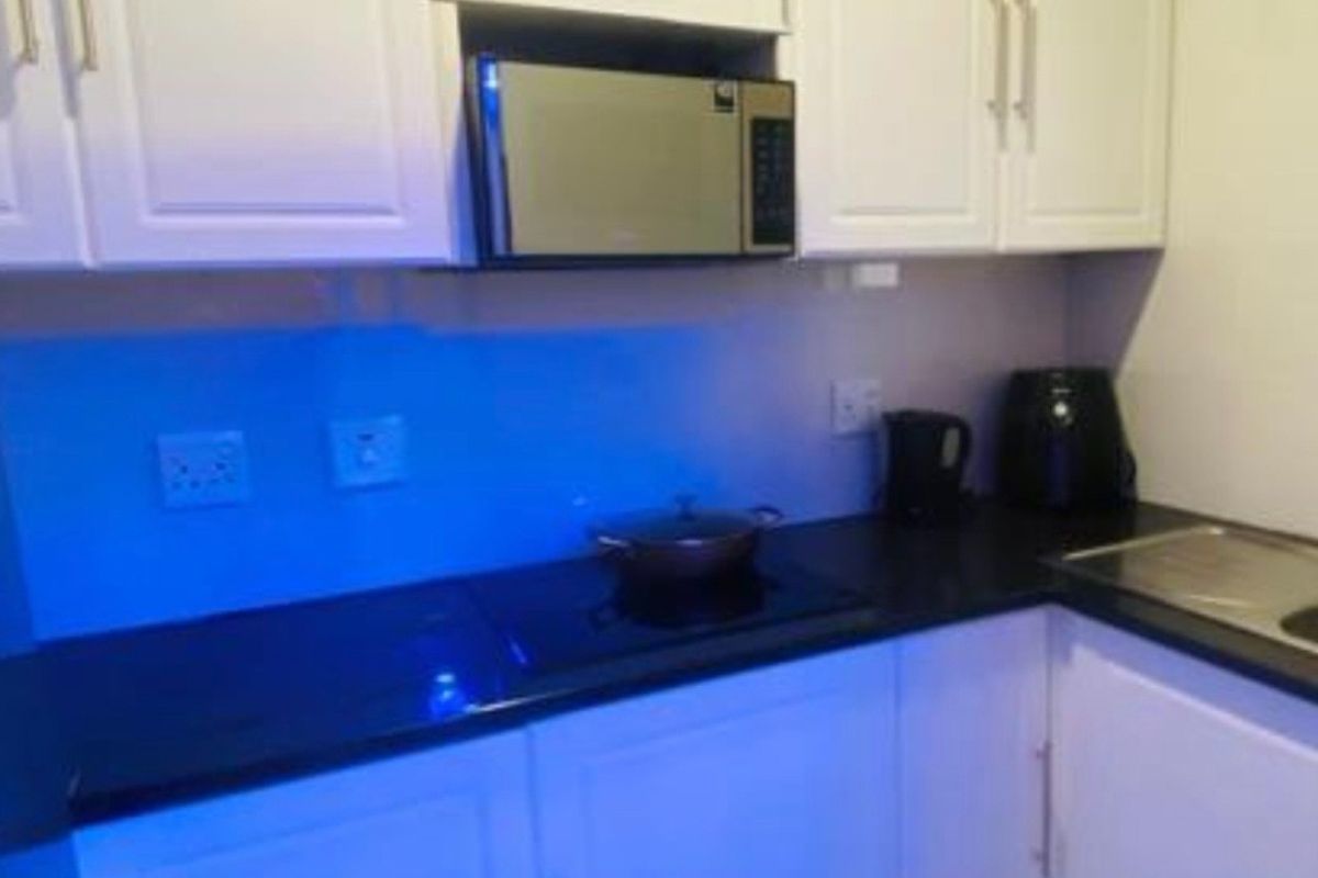 A compact kitchen featuring white cabinetry, black countertops, an integrated microwave, and an electric cooktop.