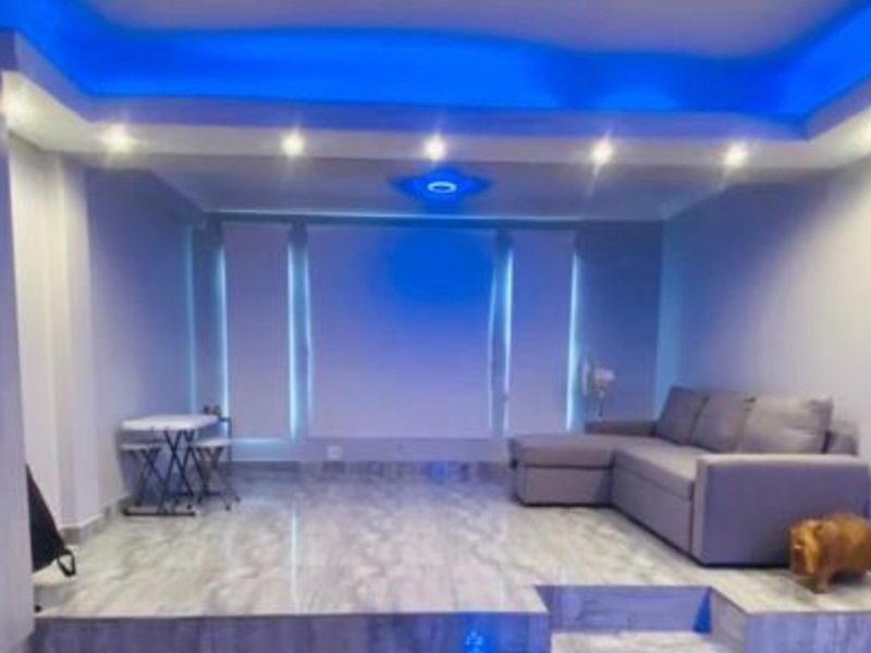 Living room featuring a raised platform area, tiled flooring, and modern recessed ceiling lighting with blue accent illumination.