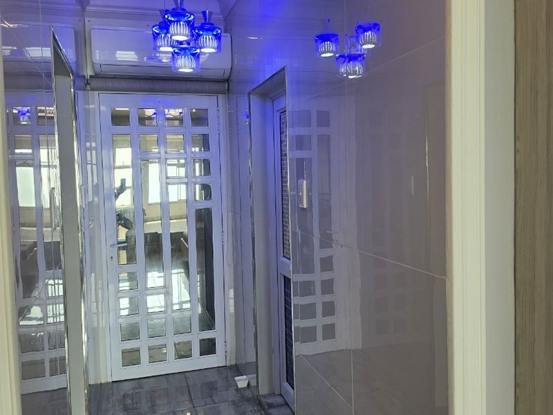 A modern, well-lit hallway featuring glossy wall tiles, tiled flooring, and a glass-panelled door, creating a bright and contemporary transition space.