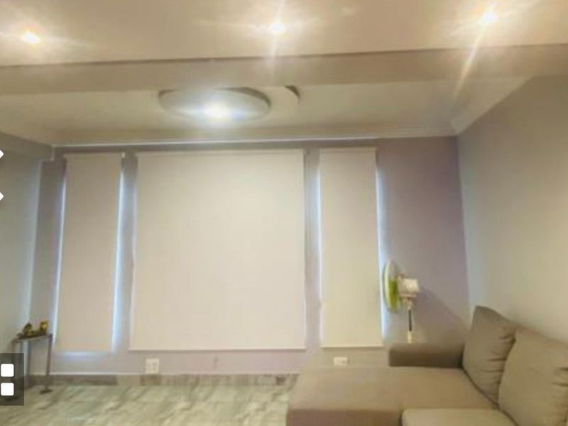 A living room featuring tiled flooring, recessed downlighting, and modern roller blinds on the windows.