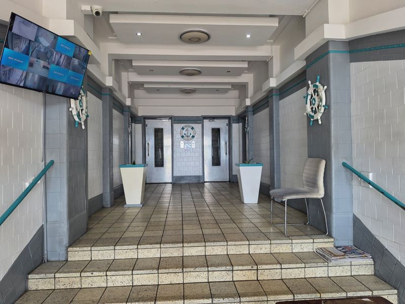 A well-maintained apartment building entrance lobby featuring tiled flooring, dual elevators, and nautical-themed wall decor.