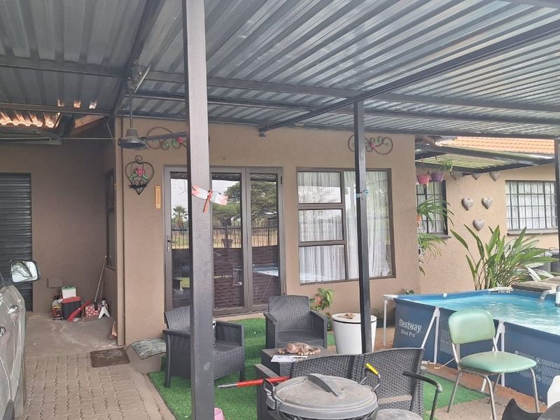 A covered outdoor patio area featuring a corrugated metal roof, steel support structure, and direct access to the home via sliding glass doors.