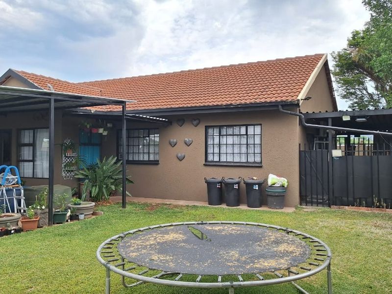 Rear view of the townhouse featuring a tiled roof, covered patio area, and a private garden space with perimeter fencing.